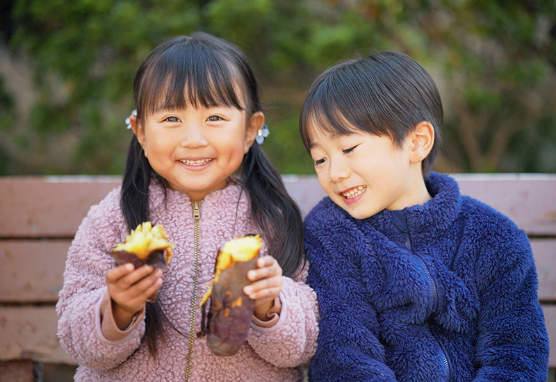 友達と仲良く芋を食べる園児